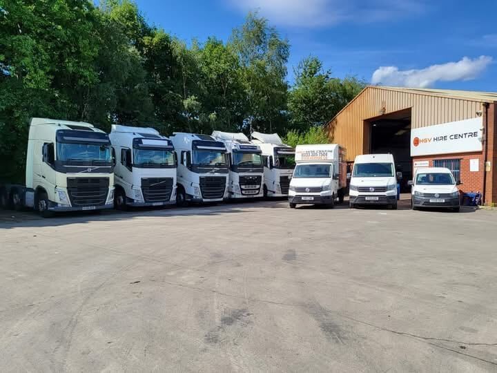 A row of white tractor units and vans parked outside the HGV Hire Centre workshop