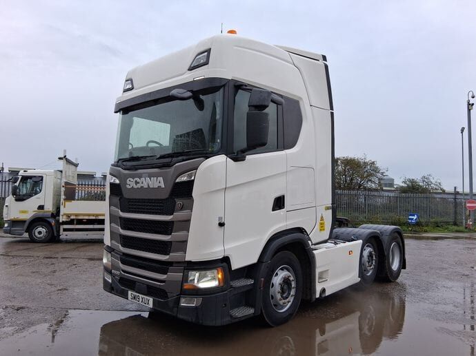 A white Scania tractor unit with a high sleeper cab, on a wet yard