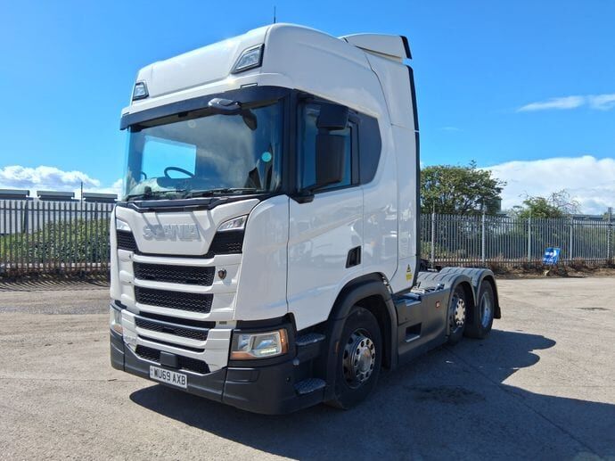 A white Scania tractor unit with a sleeper cab, under a blue sky